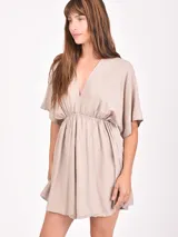 Monoprenda corta de color beige claro, con escote en V profundo, mangas cortas tipo kimono y cintura elástica fruncida.