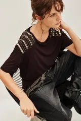 Remera de viscosa color negro, con cuello redondo y mangas cortas. Presenta un detalle decorativo de apliques metálicos en forma de corazón dispuestos en líneas sobre los hombros.