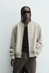 Cazadora bomber negra de corte regular fit, confeccionada en tejido efecto ante. Cuenta con cuello, puños y bajo en rib elástico, manga larga, bolsillos de vivo en la cadera y un bolsillo interior. Cierre frontal con cremallera.