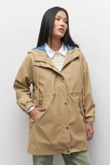 Piloto verde militar de manga larga con capucha y forro de color amarillo. Cuenta con dos bolsillos laterales con solapa, cordones ajustables, elástico en los puños, cierre y botones metálicos.