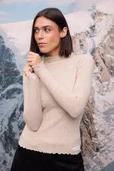 Polera de tejido de punto fino color blanco, con cuello alto, mangas largas y terminaciones con detalle de ondas en puños, cuello y ruedo.