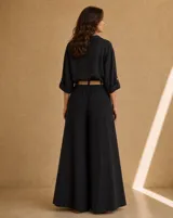 Camisa de lino negra, de corte amplio y relajado, con cuello camisero, bolsillo ojal en el pecho, mangas largas con presilla para arremangar y botones de nácar en la parte frontal.