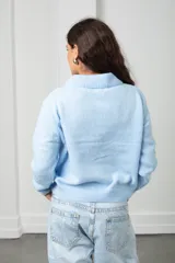 Saco tejido de punto color celeste, con cuello tipo polo, cierre frontal con botones a tono y diseño con flores bordadas en relieve. Posee mangas largas con puños acanalados y ruedo elástico.