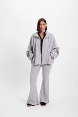 Campera holgada de felpa color gris, con cuello alto, cierre frontal completo, mangas tipo murciélago y bolsillos laterales.