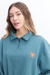 Buzo de felpa color crudo con cuello alto, cierre metálico y bordado de un corazón con rayos en el pecho.