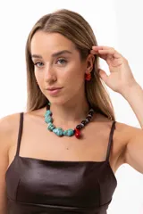Collar de diseño irregular compuesto por una mitad de cuentas de piedra turquesa y la otra mitad de cuentas de madera, piedras naturales y acrílico, con un dije central en forma de gota roja.