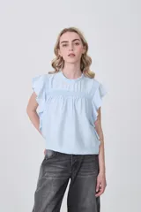 Blusa celeste de viscosa con diseño holgado, cuello a la base con detalle de volados, mangas cortas con volados y detalle de punto smock en el pecho.