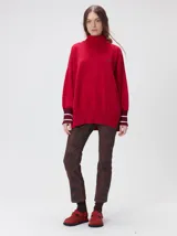 Pullover rojo de cuello alto, corte holgado, mangas largas y puños acanalados en tono burdeos con rayas blancas. Presenta un pequeño logo bordado en el pecho.