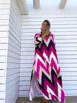 Vestido camisero largo con diseño de estampado chevron en colores fucsia, beige y negro. Presenta cuello camisero, cierre frontal con botones y mangas tres cuartos.