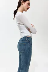 Jean de tiro alto y corte bootcut, confeccionado en denim de algodón levemente elástico con lavado azul medio y efecto desgastado. Presenta diseño clásico de cinco bolsillos, cierre de cremallera y botón metálico.