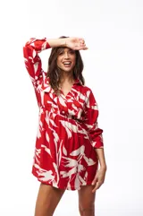 Vestido corto tipo camisero color rojo con estampado de hojas blancas, cuello camisero, cierre frontal con botones, mangas largas y elástico en la cintura.