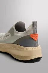 Zapatilla deportiva sin cordones de diseño técnico, con parte superior de tejido de punto transpirable en color beige. Presenta refuerzos de material protector en puntera y talón, entresuela de espuma con tecnología de rebote y suela de goma. Incluye tirador posterior para facilitar el calce.