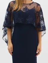 Vestido largo de corte sirena en color azul marino, confeccionado en tejido de punto con caída fluida. Presenta una capa integrada de tul fino sobre los hombros y espalda, decorada con bordados florales a tono y lentejuelas brillantes. Posee escote redondo y cierre invisible en la espalda.