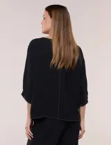 Blusa oversize color negro con caída fluida, escote redondo, bolsillo frontal en el pecho, mangas tres cuartos de hombro caído y costuras a la vista en contraste.