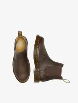 Bota Chelsea Dr. Martens 2976 YS Crazy Horse, color marrón, fabricada con cuero Crazy Horse desgastado. Presenta paneles elásticos laterales, costuras amarillas Goodyear y una tira de tela amarilla con el logo de la marca en la parte trasera.