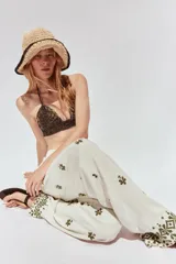 Pantalón color crema de tiro medio con cintura elástica ajustable y bolsillos delanteros. Presenta bordados florales en negro y corte ancho.