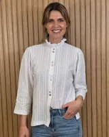 Camisa blanca de algodón con diseño de rayas verticales bordadas en relieve y detalles ajurados. Cuenta con cuello alto con volados, mangas tres cuartos y cierre frontal de botones.