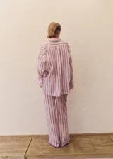 Camisa de corte oversize confeccionada en tejido de ramio, con diseño de rayas verticales en tonos rosados y oscuros. Presenta cuello camisero clásico, cierre frontal con botones y mangas largas con puños.