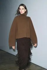 Falda midi de tiro medio, color marrón oscuro, con detalle de flecos en todo el ruedo y textura plisada o arrugada en capas horizontales. Cierre con cremallera oculta en costura.