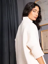 Polerón negro de tejido de punto con cuello alto, diseño oversized, mangas 3/4 y corte asimétrico más largo en la parte posterior.