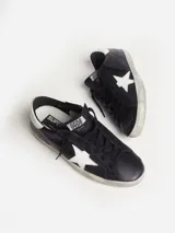 Zapatillas urbanas Golden Goose modelo Super-Star, color negro con estrella blanca en el lateral, detalle trasero en cuero blanco y suela con efecto desgastado.