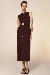 Vestido midi sin mangas de cuello redondo, con cierre frontal de botones dorados y cinturón integrado con hebilla metálica. Presenta bolsillos delanteros con solapa y una abertura en el bajo frontal.
