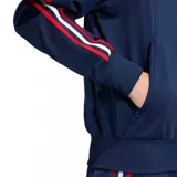Chaqueta deportiva Adidas Firebird TT C color azul marino, con cierre frontal y cuello alto. Presenta las tres franjas características de Adidas en las mangas, combinando rojo, blanco y azul. El logo del trébol de Adidas está bordado en dorado en el pecho.