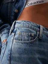 Pantalón de jean celeste de corte recto, tiro alto y pierna estrecha en el tobillo. Confeccionado en denim rígido de algodón y algodón reciclado. Diseño de cinco bolsillos y bragueta con cremallera. Logo de Calvin Klein bordado en la parte trasera de la cintura.