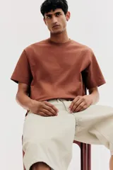Remera marrón de algodón pesado, corte holgado, cuello redondo ribeteado, hombros caídos y bajo recto.