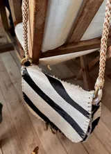 Cartera tipo bandolera de cuero con diseño de pelo estampado estilo cebra, solapa frontal, costuras visibles en los bordes y correa trenzada.