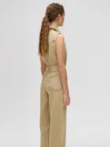 Mono largo de denim azul con corte holgado, recto en las piernas y entallado en el tronco. Tiene cuello camisero, cierre frontal con cremallera y cinturón ajustable.