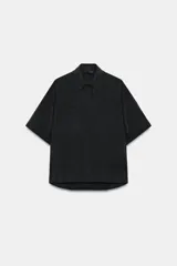 Camisa de manga corta con cuello solapa, cierre frontal con botones ocultos y bolsillos de plastrón en el delantero. Presenta un diseño con bajo asimétrico y mangas con dobladillo.