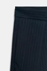 Pantalón de tiro medio de corte wide leg, confeccionado en mezcla de lyocell con patrón de rayas diplomáticas. Presenta bolsillos laterales ocultos, pliegues delanteros marcados y cierre frontal con cremallera, botón y ganchos metálicos.