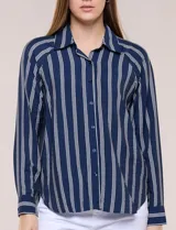Camisa de crepe blanca con rayas verticales negras, cuello camisero, mangas largas raglán y cierre frontal con botones.