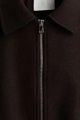 Campera corta marrón oscuro de mezcla de lana, con cuello camisero, cierre frontal plateado, bolsillos ribeteados y cordón ajustable en el bajo con dobladillo fruncido. Diseño oversized con hombros caídos y mangas largas.