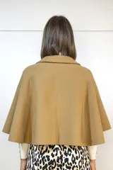 Capa de paño color camel con diseño de doble botonadura frontal y solapas clásicas. Presenta un corte estructurado y mangas abiertas tipo capa que ofrecen libertad de movimiento.