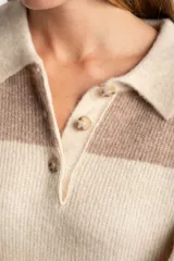 Sweater de tejido de punto color blanco roto o crema, con textura jaspeada. Presenta cuello polo y un escote con tres botones nacarados. El calce es holgado (oversize) y tiene mangas largas.