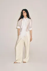 Camisa blanca de tejido semitransparente ZARA Woman Collection, con cuello redondo, manga corta y detalle de pañuelo integrado en el mismo tejido al cuello. Cierre frontal con botones.
