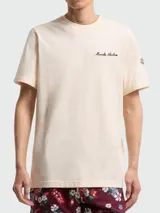 Remera de algodón color beige con cuello redondo, manga corta y bordado con la inscripción "Moncler Archive" en el pecho. Presenta un parche con el logo de la marca en la manga izquierda.