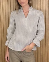 Blusa color lila con estampado vertical de ramas y hojas blancas, cuello alto con volados y escote en V. Presenta mangas largas abullonadas con puños elastizados.