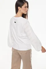 Blusa blanca de calce recto y relajado, con mangas largas abullonadas de broderie y puños ajustados.