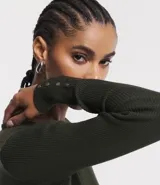 Suéter de punto color rosado, con cuello barco, mangas largas y puños con botones decorativos. El dobladillo también es acanalado.