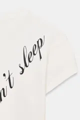 Camiseta blanca de manga corta y cuello redondo, con estampado en tipografía cursiva negra que dice "Creativity doesn't sleep" en diagonal.