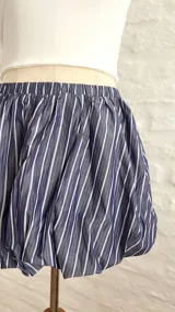 Pollera corta estilo globo, color azul marino con rayas verticales blancas, con cintura elástica.