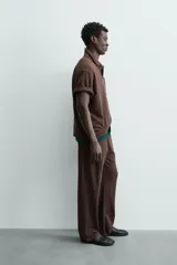 Polo de hombre de corte relajado, color marrón oscuro, confeccionado en tejido texturizado con rayas verticales. Posee cuello solapa y cierre frontal con botonadura oculta por solapa.