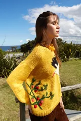 Sweater tejido de lana color amarillo con bordado de cigüeña en el frente y detalle floral en la manga.