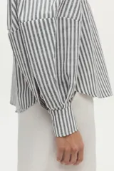 Camisa de algodón con rayas verticales grises y blancas, cuello camisero, mangas largas abullonadas y cierre frontal con botones.