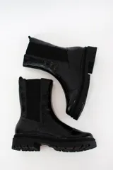 Bota tipo chelsea de cuero acharolado negro, con elásticos laterales y suela track dentada.