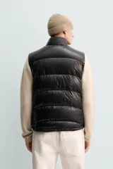 Chaleco acolchado de corte regular, confeccionado en tejido técnico repelente al agua. Presenta cuello subido, cierre frontal de cremallera, bolsillos laterales con cierre oculto y bajo ajustable con elástico. Relleno de plumón y pluma.