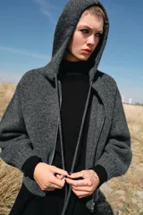 Chaqueta de punto con capucha, manga larga y cierre frontal con cremallera metálica. Presenta un diseño de tejido texturizado en color gris oscuro con detalles en contraste en los puños.
